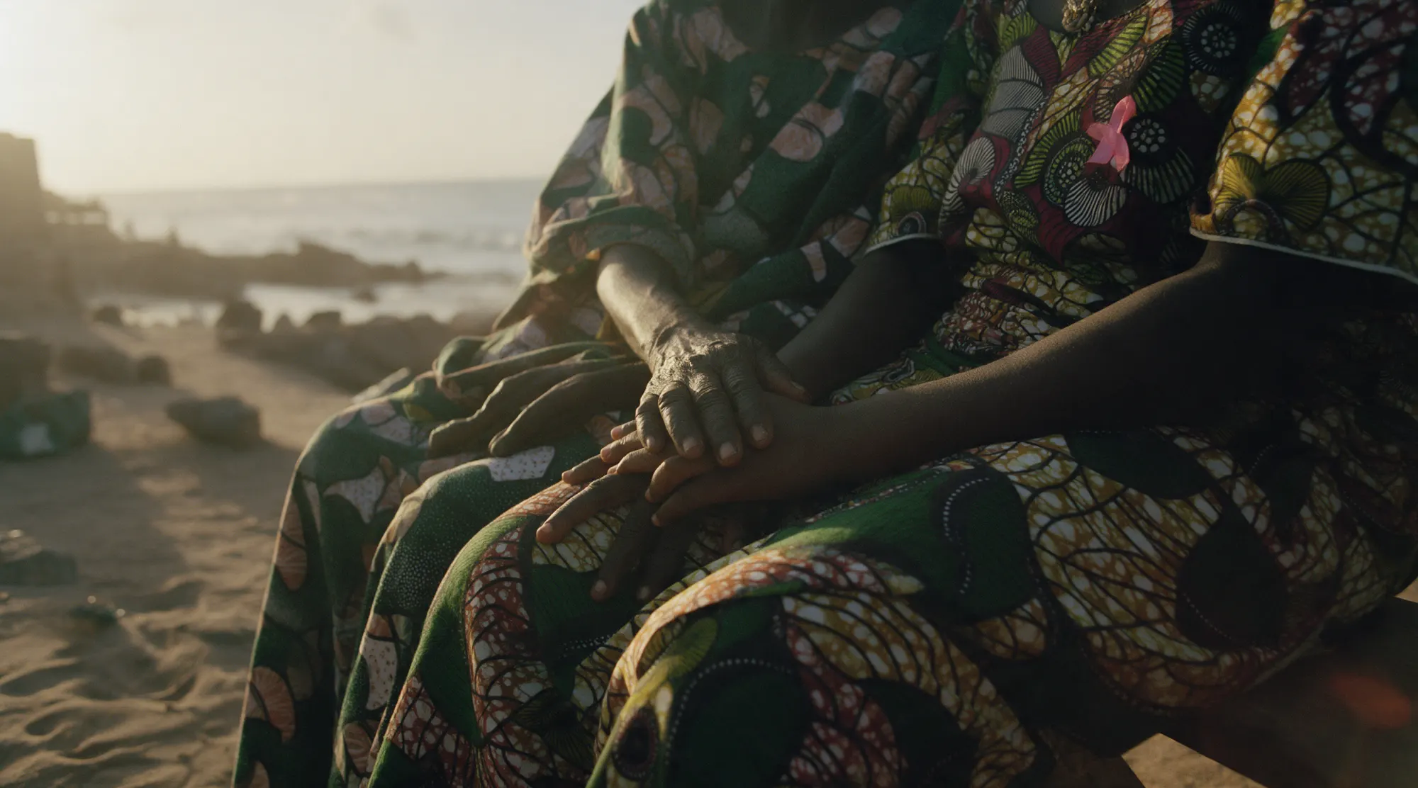 Les mains de trois générations de femmes posées les unes sur les autres, sur des pagnes en wax.